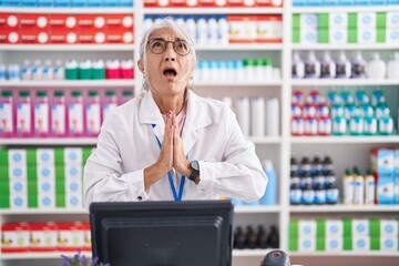 Middle age woman with tattoos working at pharmacy drugstore begging and praying with hands together...