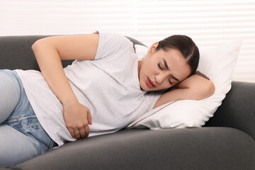 Woman suffering from abdominal pain while lying on sofa indoors. Unhealthy stomach