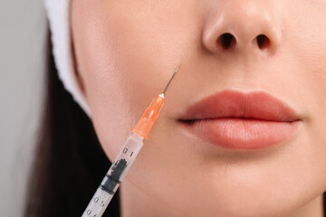Young woman getting facial injection on light grey background, closeup. Cosmetic surgery