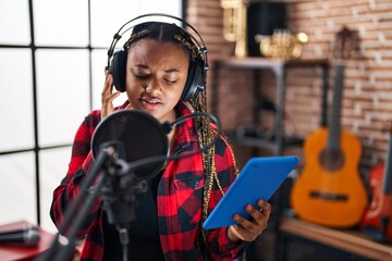 Fototapeta na wymiar African american woman musician singing song using touchpad at music studio