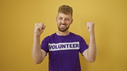 Handsome young man with beard celebrating in a 'volunteer' t-shirt against a yellow background