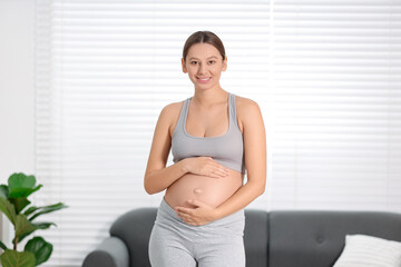 Beautiful pregnant woman standing near sofa at home