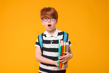 Surprised schoolboy with backpack and books on orange background