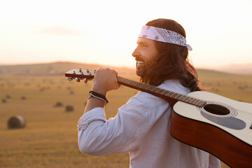 Portrait of happy hippie man with guitar in field, space for text