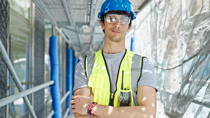 Young hispanic man architect standing with arms crossed gesture and serious face at construction place