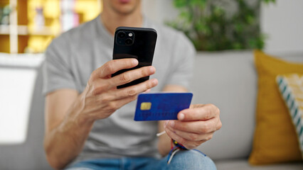 Young hispanic man make photo to credit card by smartphone at home