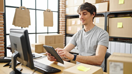 Young hispanic man ecommerce business worker using touchpad smiling at office - obrazy, fototapety, plakaty