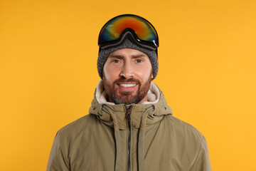 Winter sports. Happy man in ski suit and goggles on orange background