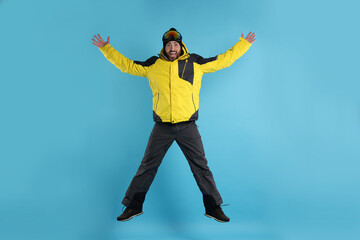 Winter sports. Man in ski suit and goggles jumping on light blue background