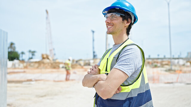 Young hispanic man architect smiling confident standing with arms crossed gesture at construction place
