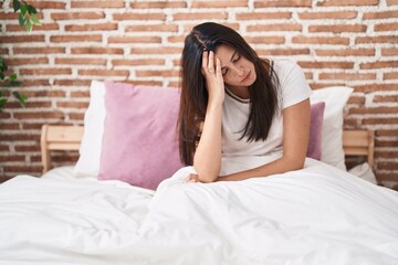 Young beautiful hispanic woman stressed sitting on bed at bedroom