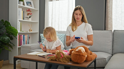 Relaxing at home, serious caucasian mother and daughter bonding over a drawing session on a notebook using their smartphone - Powered by Adobe