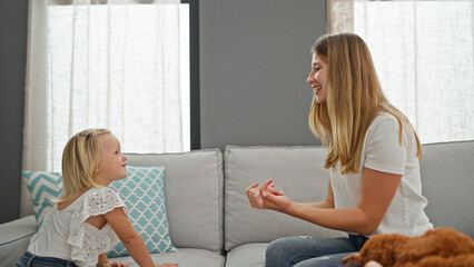 Relaxed caucasian mother and her little girl confidently sharing smiles indoors, comfortably sitting on living room sofa encapsulating family lifestyle.