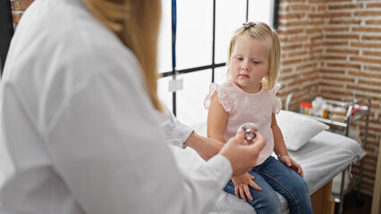 Caring pediatrician in clinic examining adorable kid patient's chest using stethoscope, ensuring...