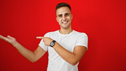 Handsome young hispanic man smiling and pointing on a red isolated background wearing a watch