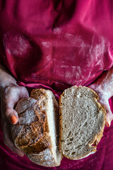 Obraz premium Woman in red apron proudly shows her freshly baked bread cut in two parts. Irresistible aroma.