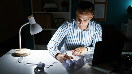 Hispanic young man working late in office, illuminating designs with desk lamp