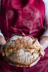 Woman in red apron proudly displays her freshly baked bread. Irresistible aroma.