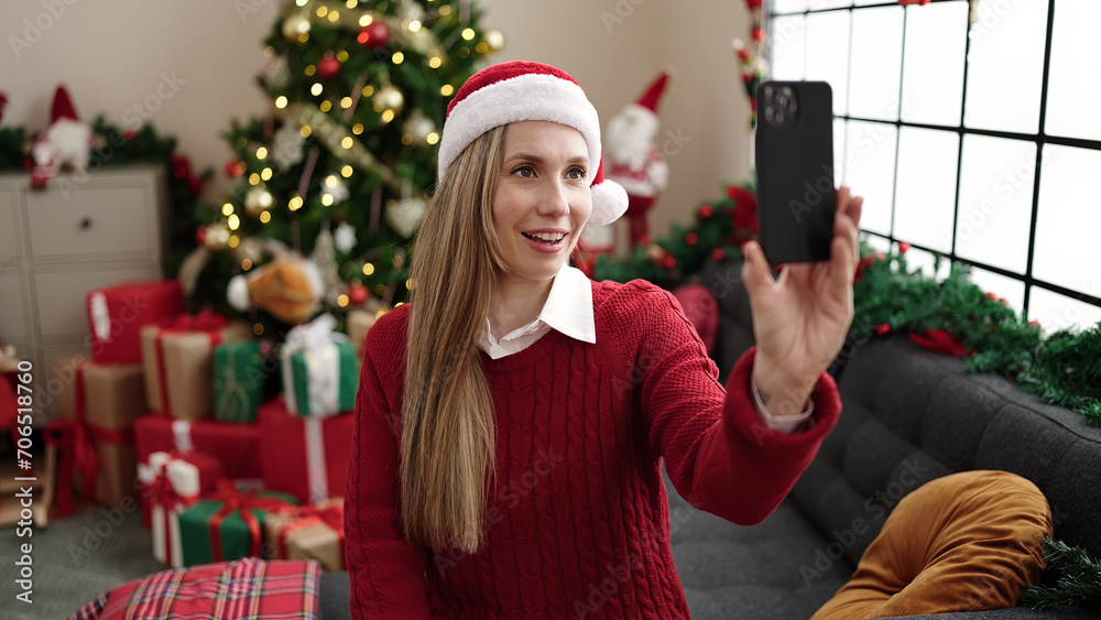 Sticker Young blonde woman make selfie by smartphone sitting on sofa by christmas tree at home