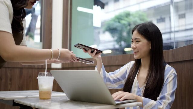 Asian customer using smartphone scanning bar code to pay through banking app with waiter at cafe restaurant, cashless QR code technology and money transfer concept