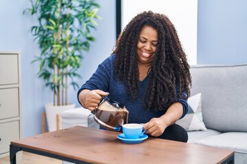 African american woman pouring coffee on cup sitting on sofa at home