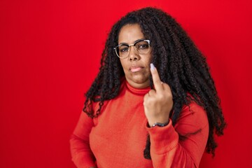 Plus size hispanic woman standing over red background showing middle finger, impolite and rude fuck...