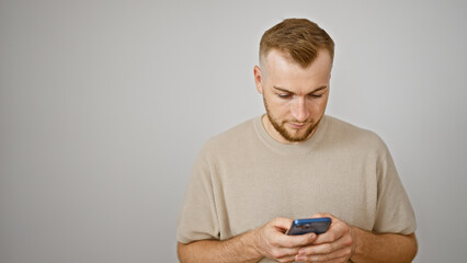 A focused caucasian man with a beard texts on a smartphone against an isolated white background.