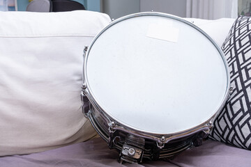 A 6.5 inch metal drum snare on the sofa with cushions.