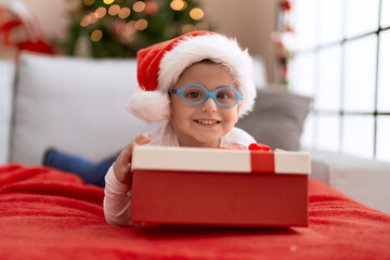 Adorable hispanic toddler lying on sofa by christmas tree holding gift at home