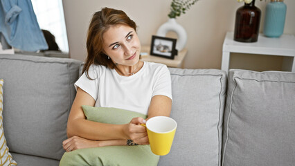 Young woman drinking coffee sitting on sofa thinking at home