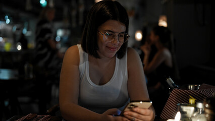 Young beautiful hispanic woman using smartphone sitting on the table at the restaurant
