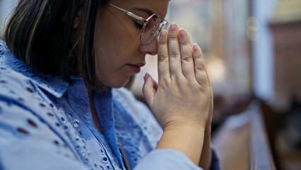 Young beautiful hispanic woman praying on a church bench at St. Karl BorromÃ¤us church - obrazy, fototapety, plakaty