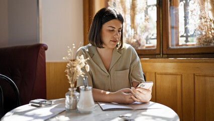 Young beautiful hispanic woman using smartphone sitting on the table at cafeteria