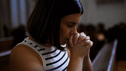 Fototapeta na wymiar Young beautiful hispanic woman praying on a church bench at Augustinian Church in Vienna