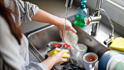 Young beautiful hispanic woman washing plates at the kitchen