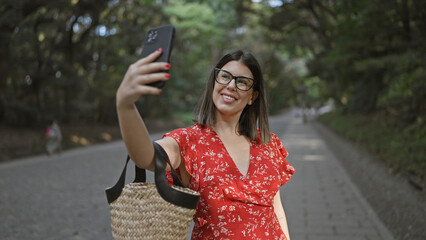 Beautiful hispanic woman in glasses having cheerful fun taking selfie picture with smartphone at famous meiji temple, tokyo