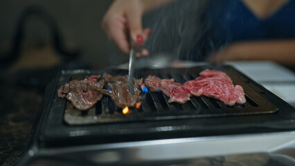 Modern dining experience, young woman's hands cook delicious, rare wagyu beef on grill in japanese...