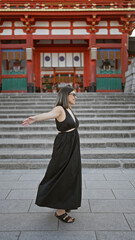 Joyful hispanic woman in glasses, embracing freedom with open arms, smiling and looking around fushimi inari taisha shrine in kyoto, japan