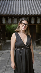 Cheerful beautiful hispanic woman, proudly posing with her glasses on, flashing a gorgeous smile at kyoto's serene kodaiji temple