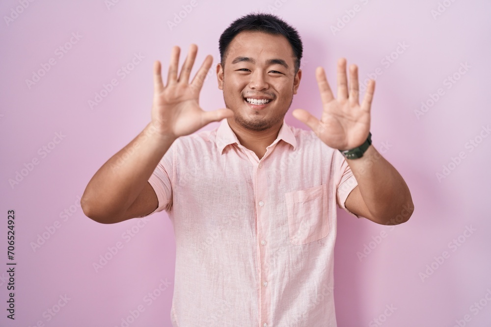 Poster chinese young man standing over pink background showing and pointing up with fingers number ten whil