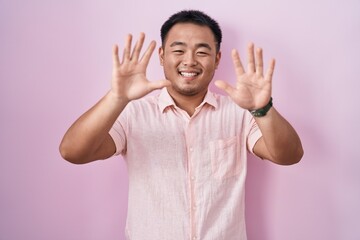 Chinese young man standing over pink background showing and pointing up with fingers number ten while smiling confident and happy.