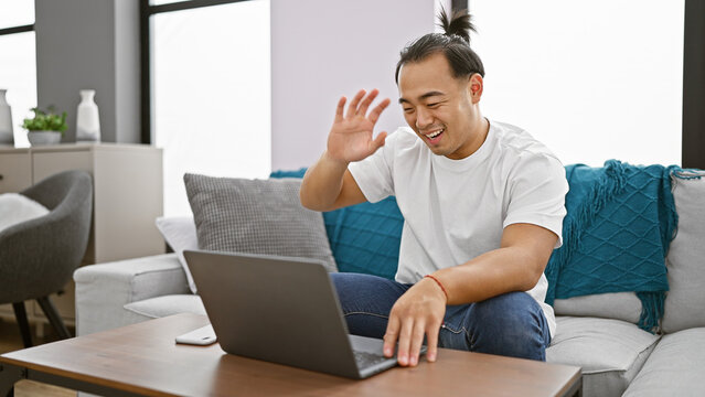 Young chinese man having video call sitting on sofa at home