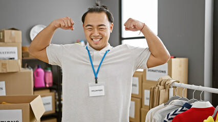 Smiling young chinese man, confidently volunteering with strong gesture in charity center, standing...