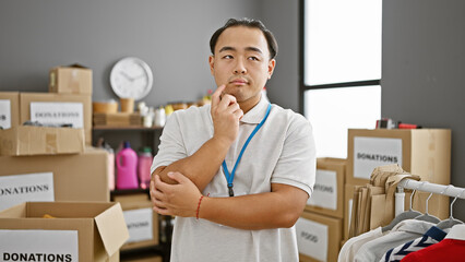 Handsome young chinese man volunteering, his serious face displaying thoughts of altruism, standing in charity center - the heart of the community