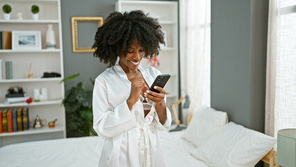 African american woman looking sexy using smartphone smiling at bedroom