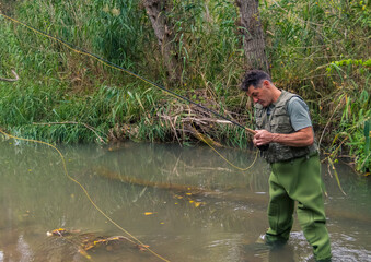 Angler in the water of a river with a wader and fly fishing rod.