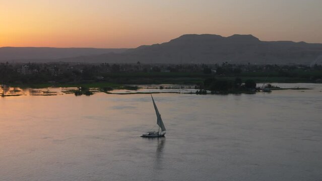 Felucca sailboat on the nile river at sunset with valley of kings in background luxor egypt