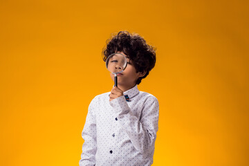 Obraz premium Child boy looking through magnifier over yellow background. Education and curiosity concept