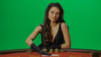 Female in studio on chroma key green screen isolated background. Woman in black dress at the blackjack poker table laying hands on the cards.