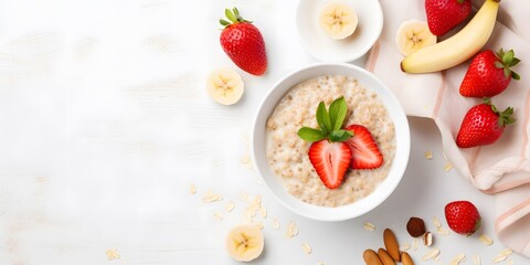 Bowl of oatmeal porridge with strawberry and banana on white table top view. Healthy and diet breakfast.